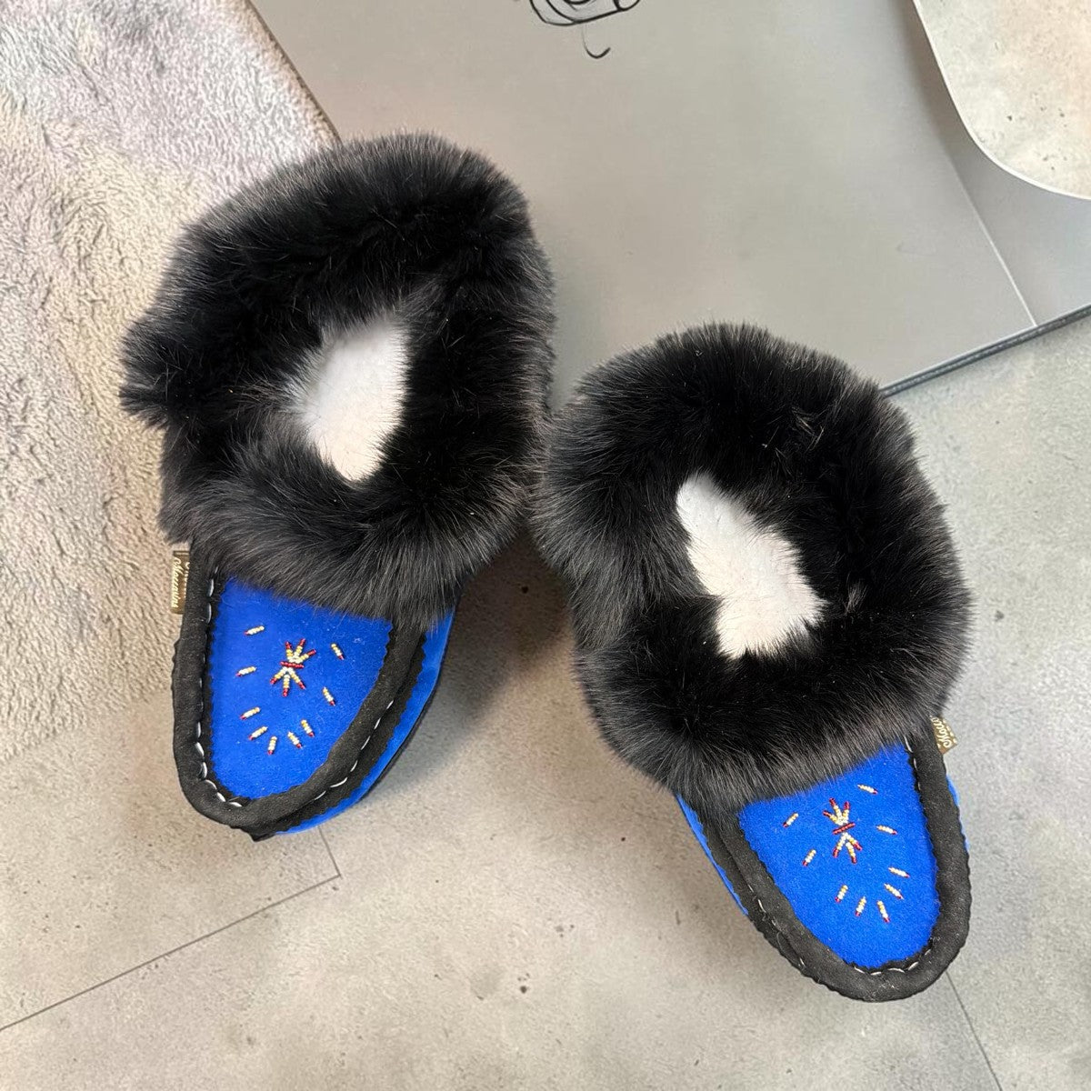 Alberta blue suede moccasin with a black rabbit fur ankle collar, handcrafted for cozy indoor comfort. Photo of upper view.