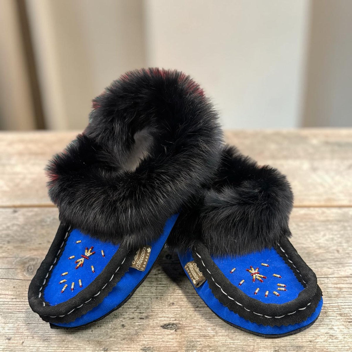 Alberta blue suede moccasin with a black rabbit fur ankle collar, handcrafted for cozy indoor comfort. Photo of front side view.