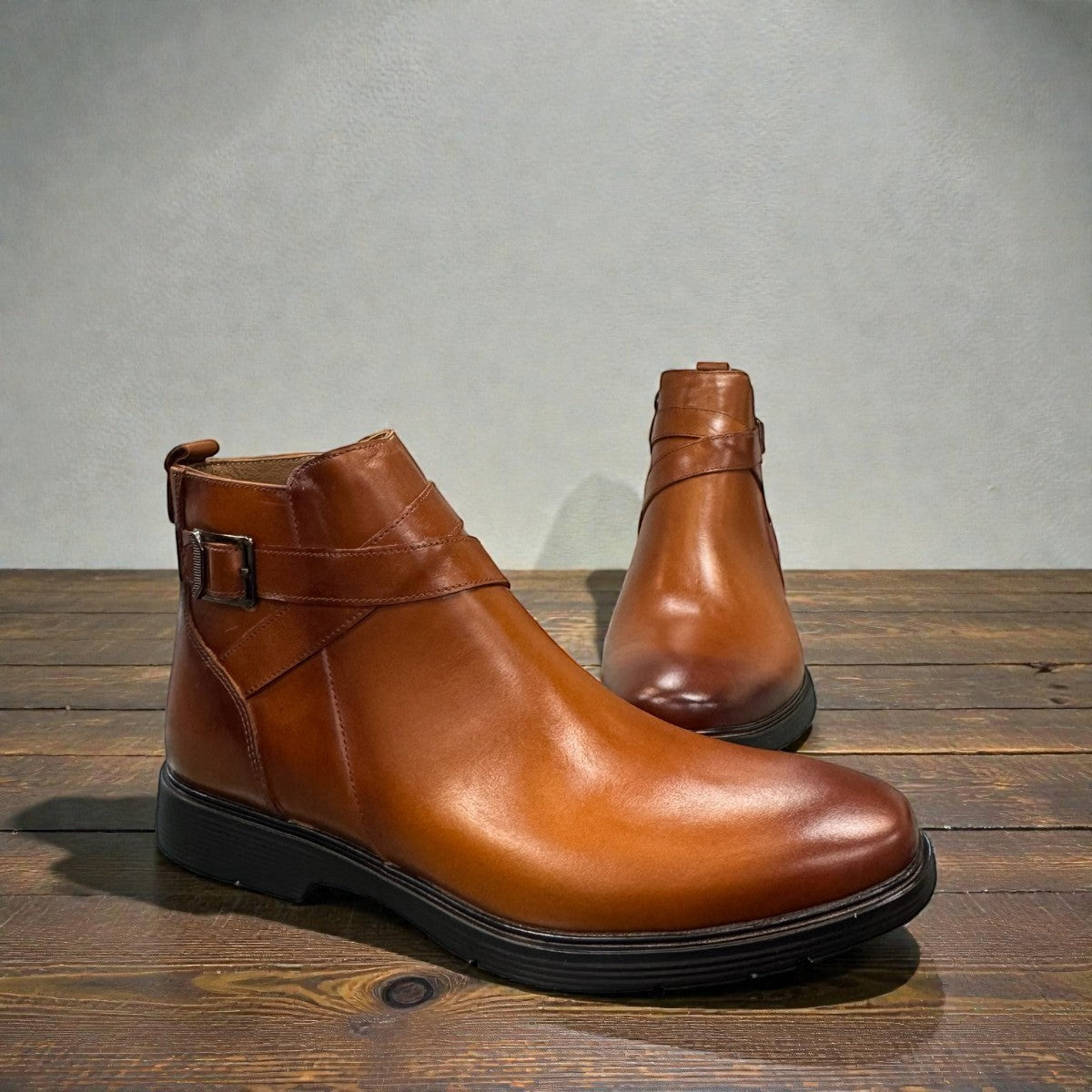 Brown leather ankle boots with a side buckle strap and durable rubber sole for formal wear. Photo of front view of sides.