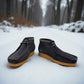 Sina Footwear blue leather Shacre boots with a Wallabee-inspired design and rubber sole, set on a snowy forest path. Photo of the sides of both shoes.