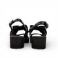 Django & Juliette black leather platform sandals featuring an oversized bow and chunky lugged sole. Photo of back view.