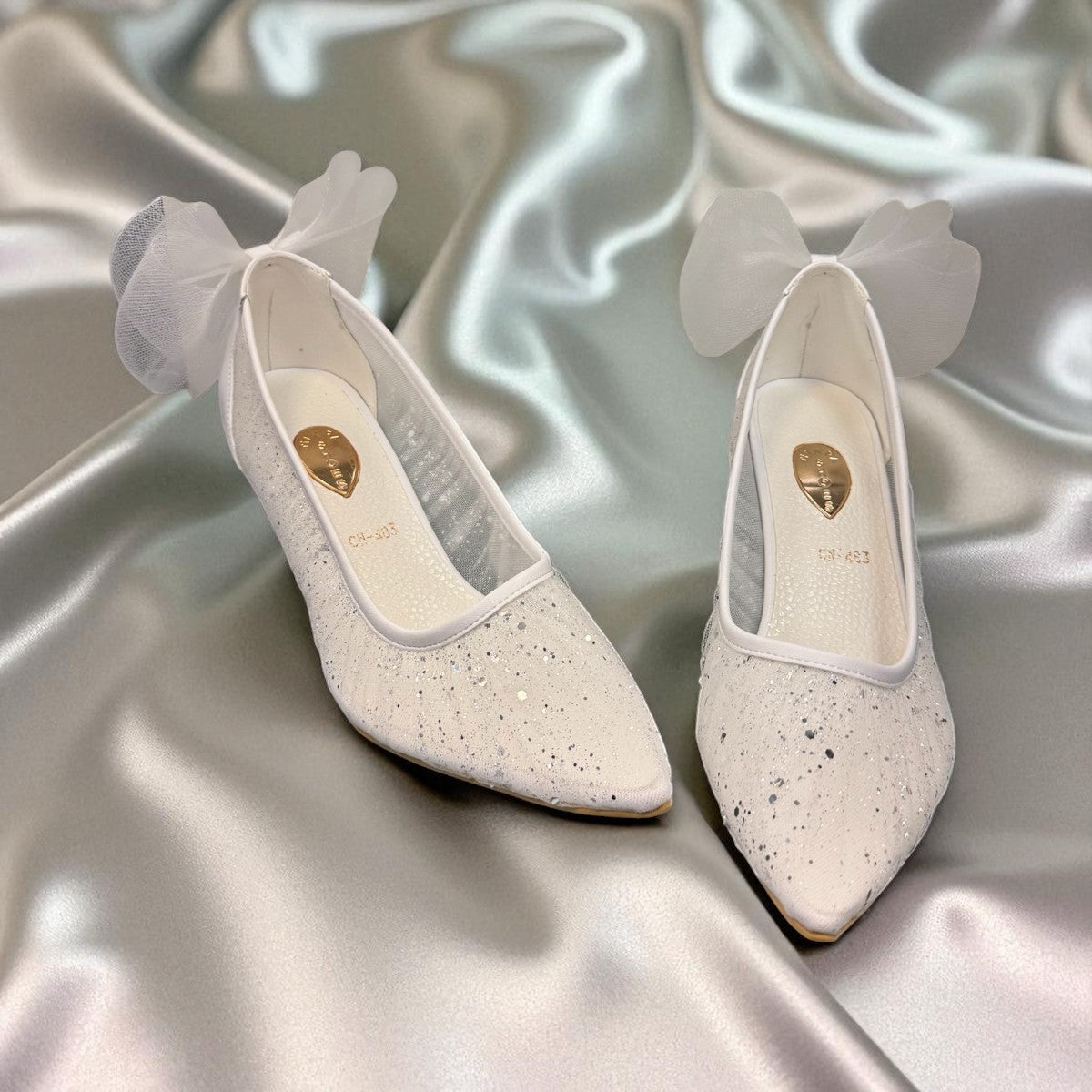 NIKPA SANA white bridal pump with glitter finish, pointed toe, and sheer tulle bow detail on the heel.