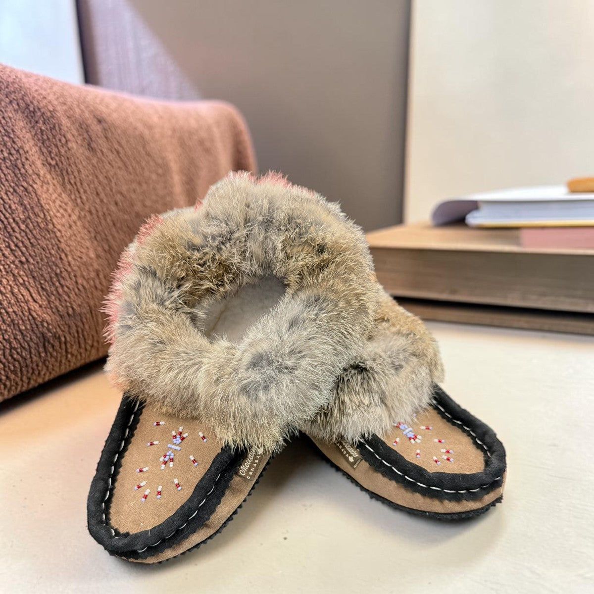 Alberta suede moccasins in coffee and black with a plush rabbit fur ankle collar and side stitching. Photo of front side view.