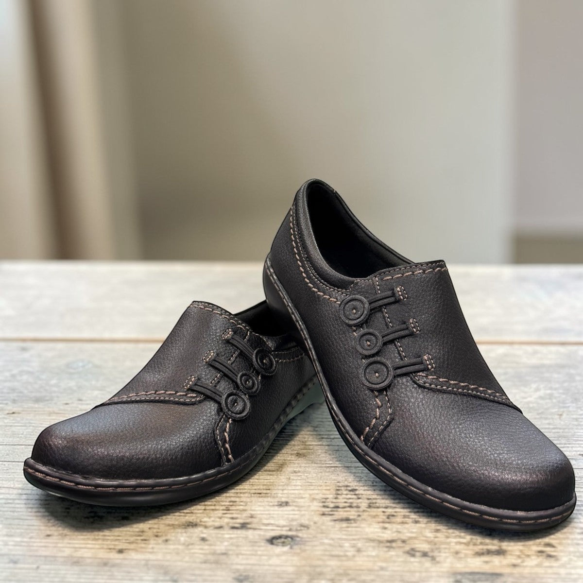 Clarks Ashland Effie black leather slip-on shoe with round toe and decorative button detail. front view.