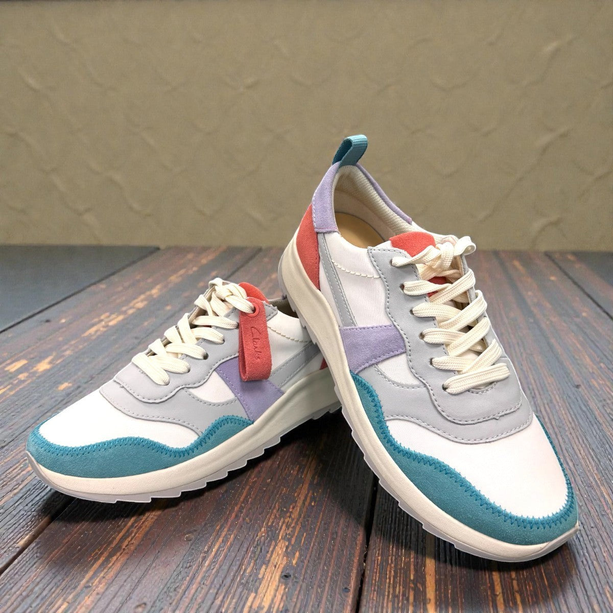 Clarks DashLite Jazz sneakers in lilac, teal, and coral leather with a retro jogger design and lace-up front. photo of the front.