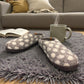 Lhasa grey wool mule slippers with white polka dots on a grey rug next to a steaming mug