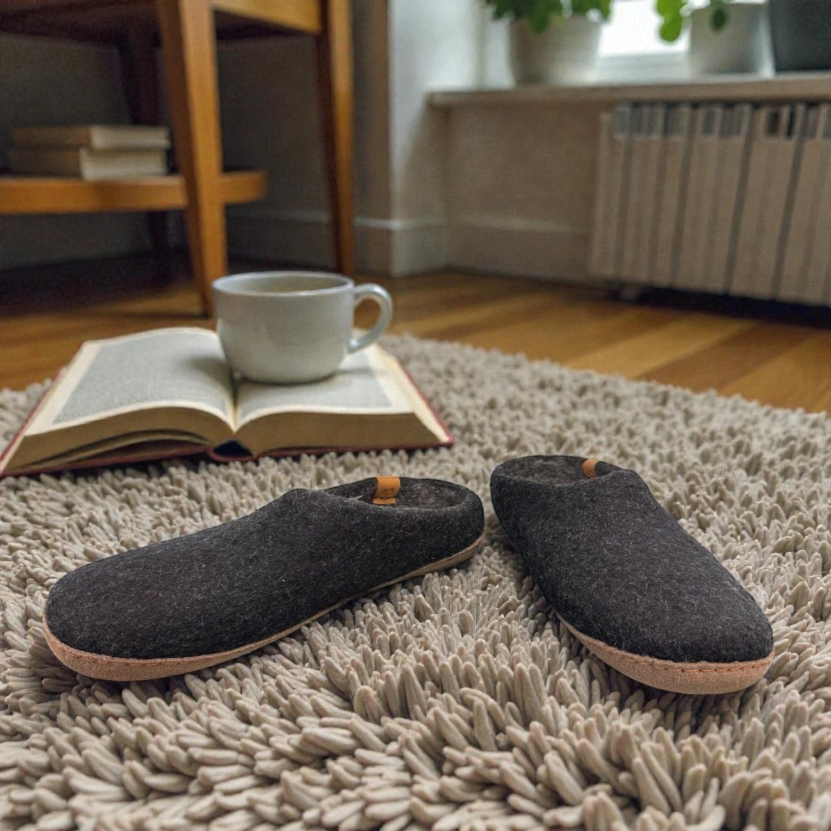 Makalu black wool slippers with EnergySole insoles resting on a cozy rug next to a book and coffee cup.
