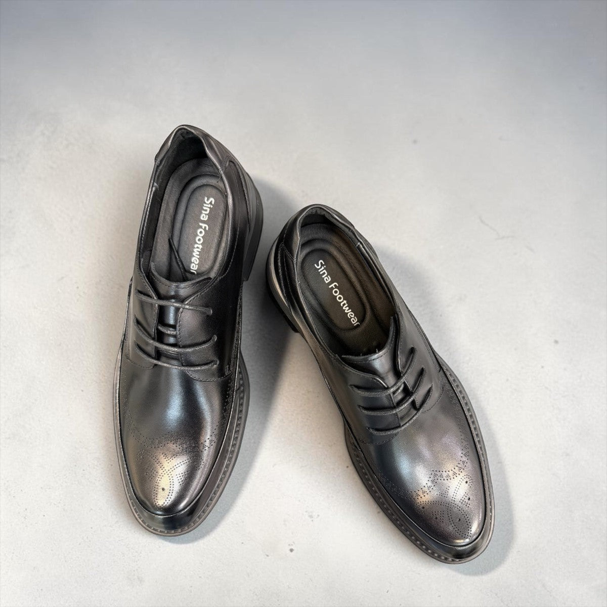 Sina Footwear black leather derby shoe with brogue-inspired perforations and a lightweight chunky rubber sole.
photo of the top side