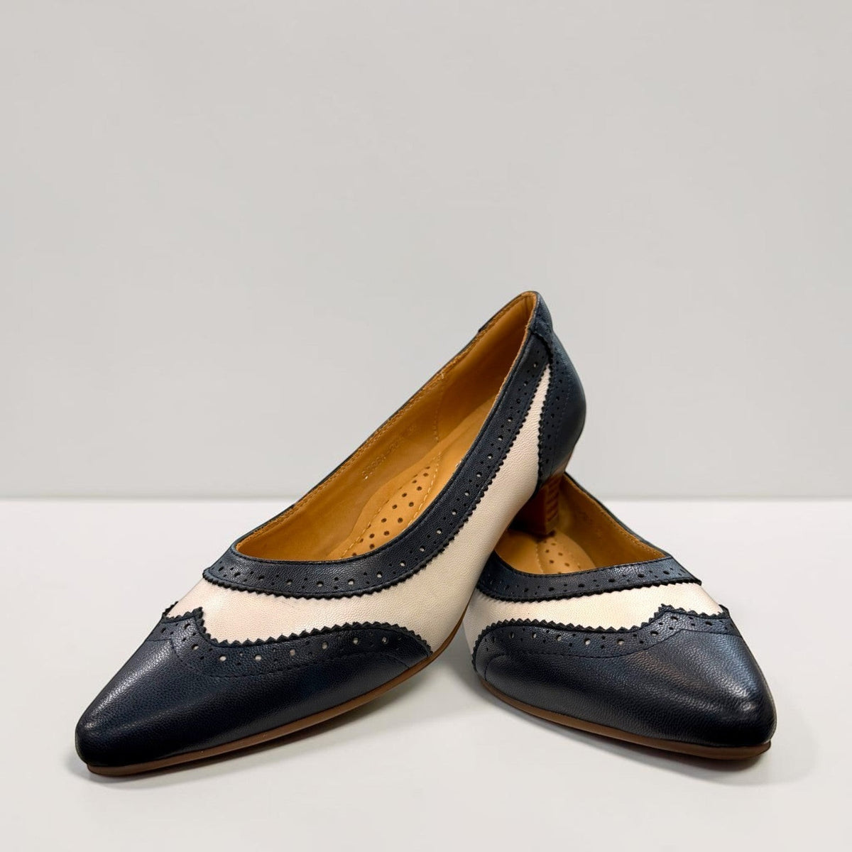 Sina Footwear navy blue and off-white leather pumps with brogue detailing, pointed toe, and low block heel.
photo of the front side