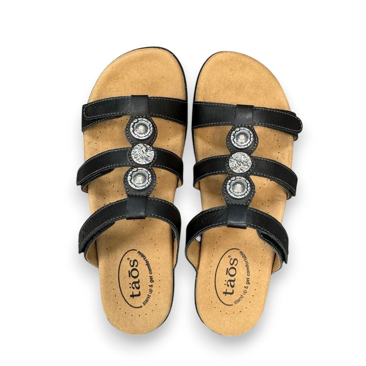 Taos Prize 4 black leather slide sandals with adjustable hook and loop straps and cushioned foot bed. Photo of upper view.