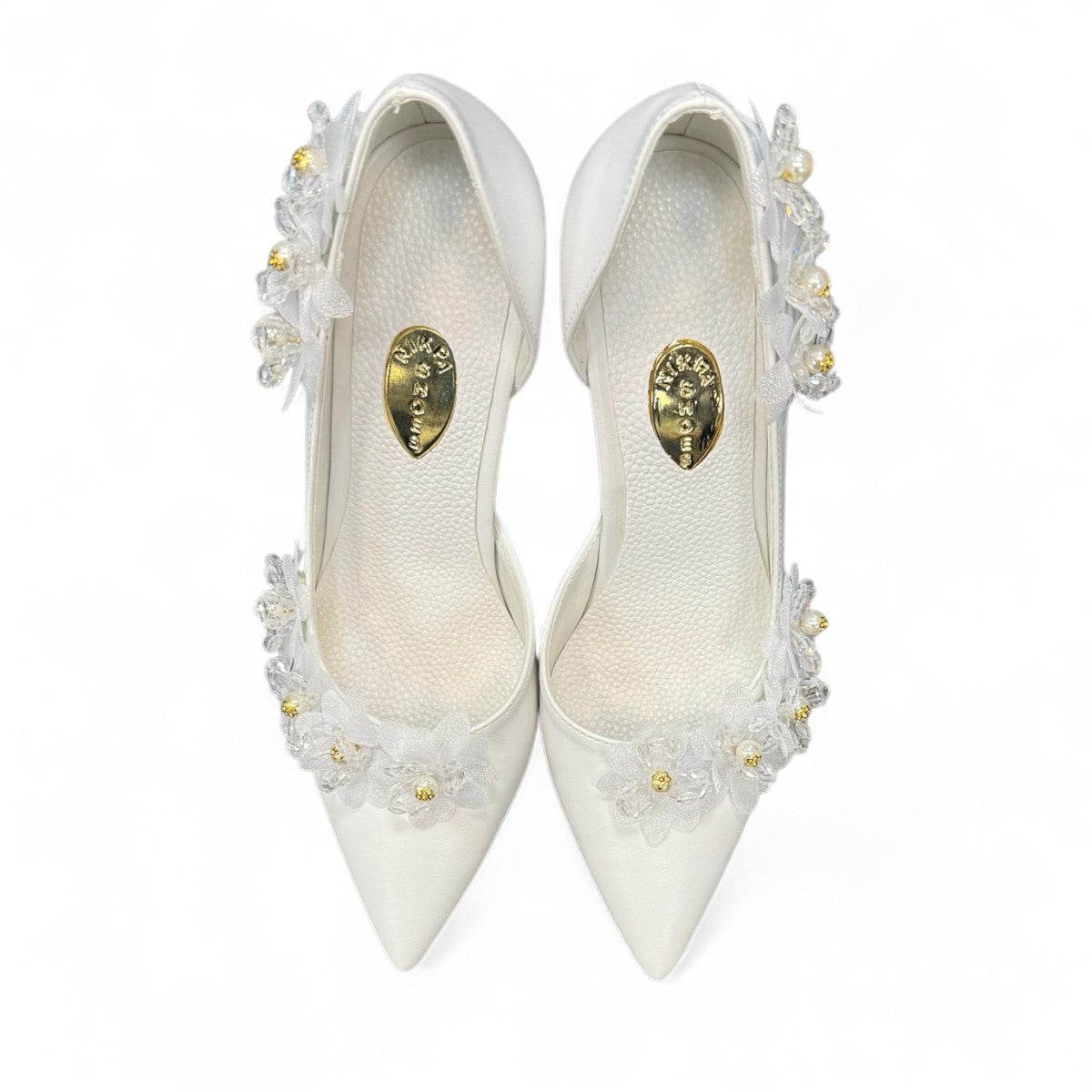 Ticky white pointed-toe high heel pump featuring delicate floral embellishments with crystal accents. Photo of upper view.