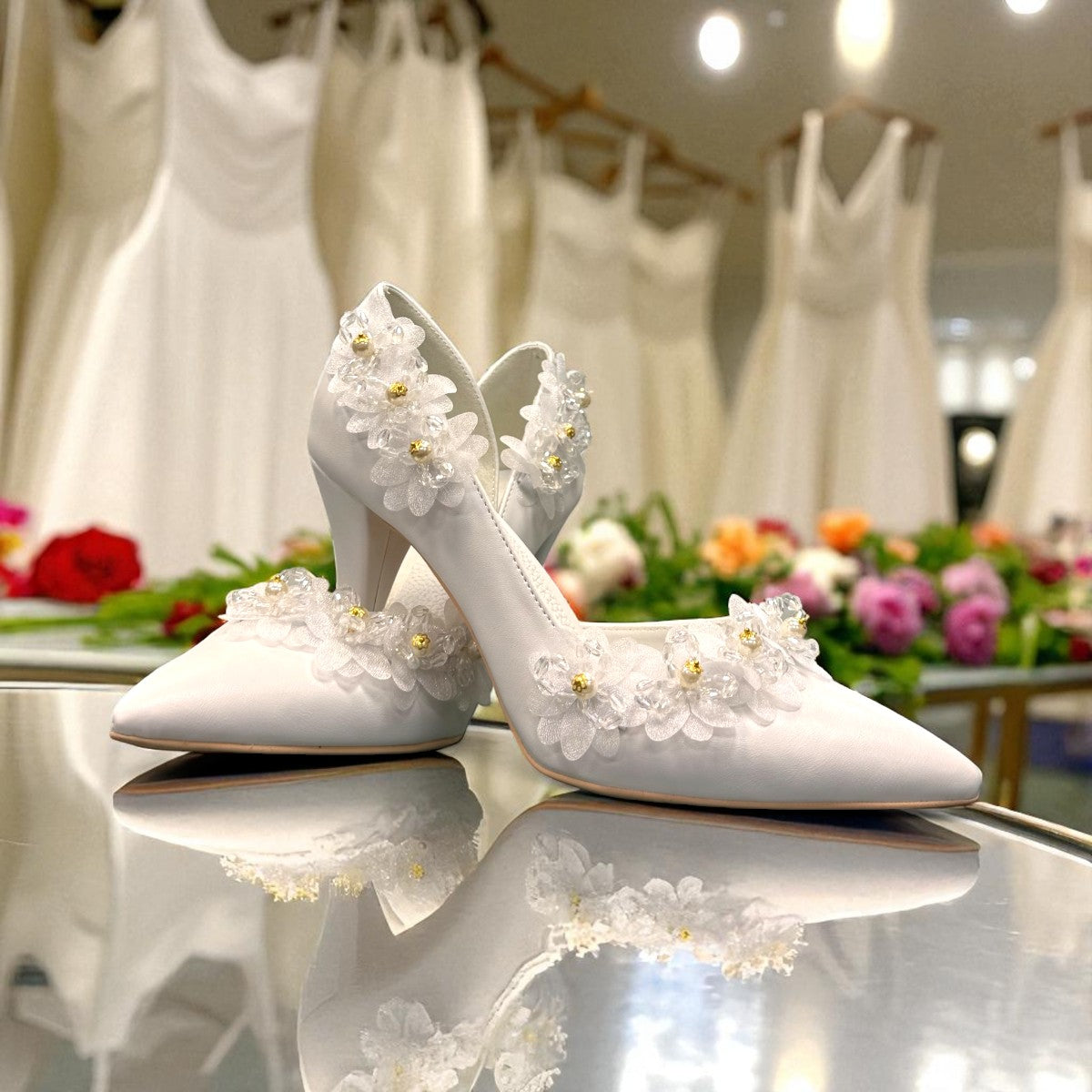 Ticky white pointed-toe high heel pump featuring delicate floral embellishments with crystal accents. Photo of front side view.