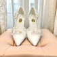 Ticky white pointed-toe high heel pump featuring delicate floral embellishments with crystal accents. Photo of front view.