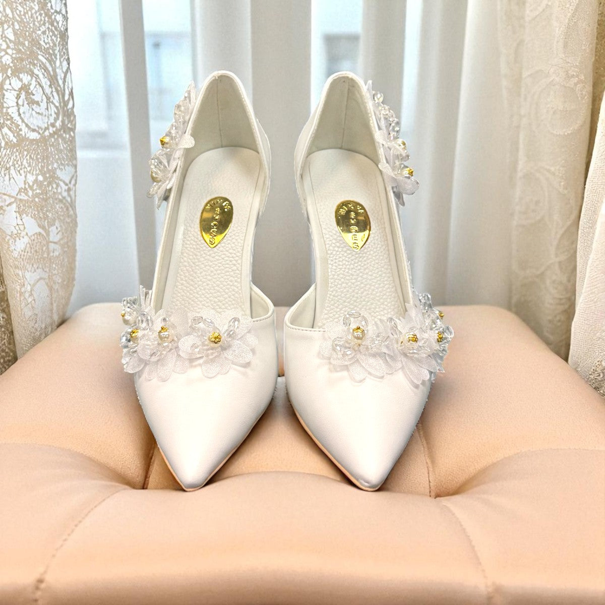 Ticky white pointed-toe high heel pump featuring delicate floral embellishments with crystal accents. Photo of front view.